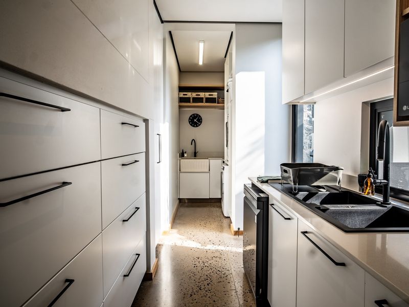 Modern, high-end scullery featuring sleek white cabinetry, polished concrete floors, composite stone countertops, and premium black fixtures with integrated appliances.