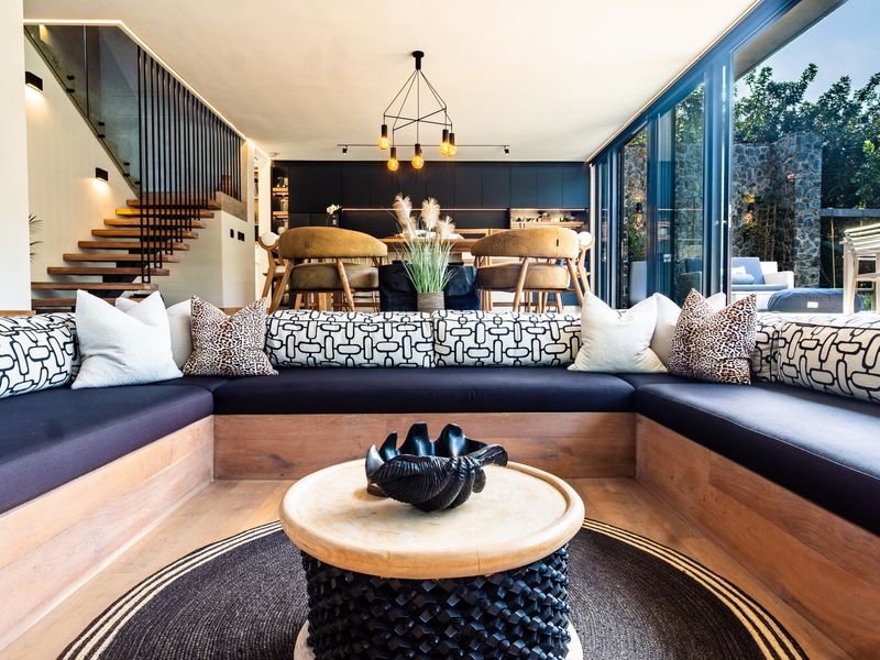 Modern open-plan living area featuring built-in timber seating, a floating staircase with metal balustrade, and expansive sliding glass doors opening to the garden.