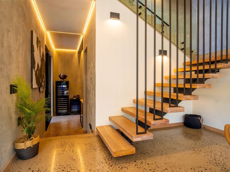 Modern hallway featuring a striking floating timber staircase with metal balustrades, polished concrete flooring, and sophisticated recessed LED accent lighting.