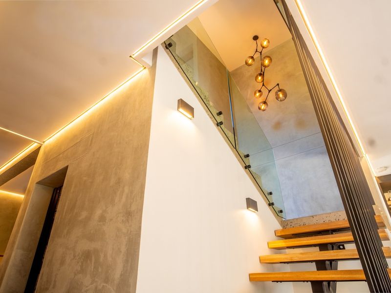 Modern hallway featuring a floating staircase with a glass balustrade, complemented by sophisticated recessed LED lighting and contemporary concrete-effect wall finishes.