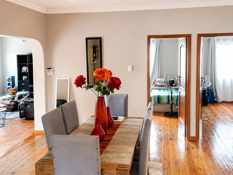 Open plan dining area featuring polished hardwood floors, connecting to a tiled living space and adjacent bedrooms through classic wooden door frames.