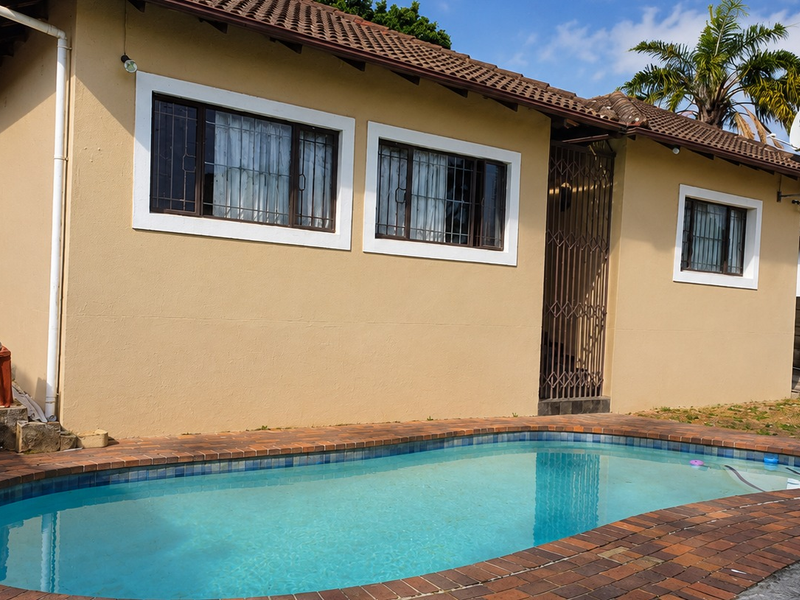 Exterior view of the property featuring a swimming pool with brick coping, tiled roof, and security features including burglar bars and gates.