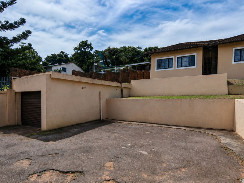 Exterior view of the property featuring a garage, paved driveway, and tiered retaining walls with a tiled roof structure.