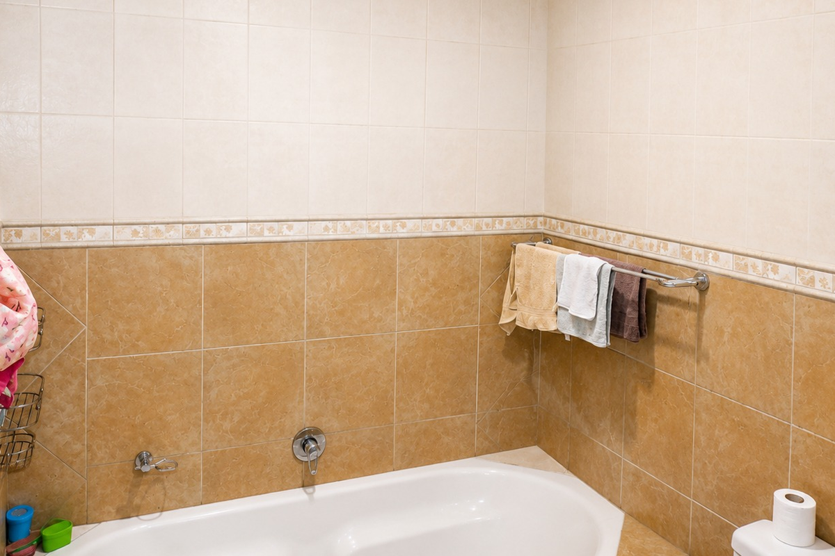 A functional bathroom featuring a built-in bathtub with chrome fixtures and two-tone ceramic wall tiling with a decorative border.