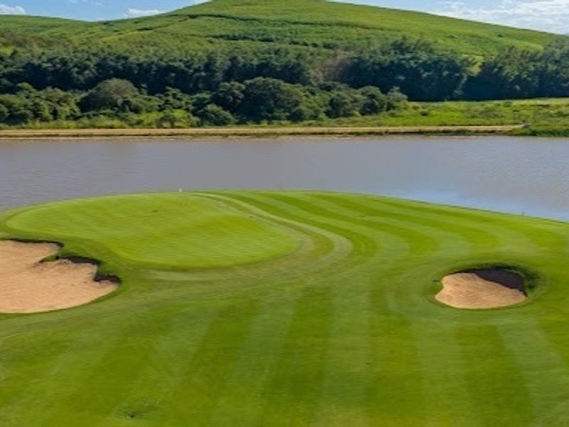 Aerial view of a manicured golf course green featuring sand bunkers, overlooking a scenic lake and rolling hills.