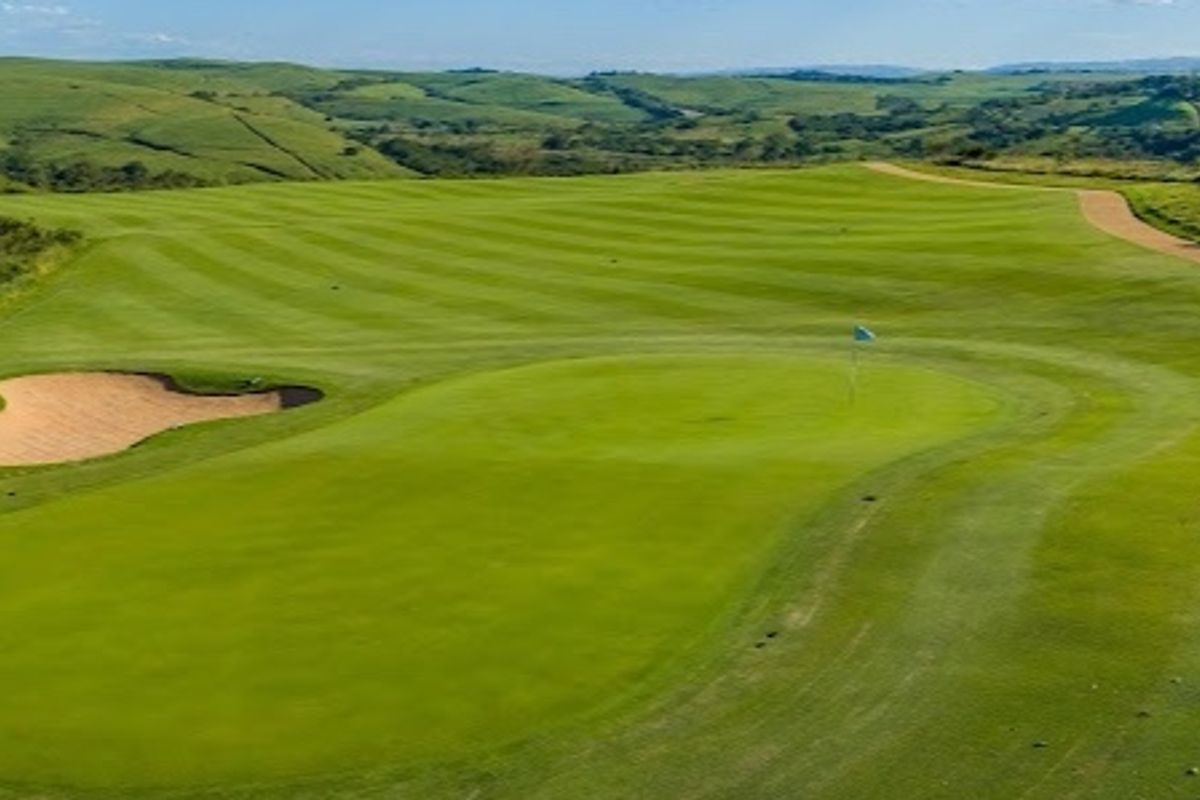 An elevated view of a well-maintained golf course green with a sand bunker and rolling hills in the background.