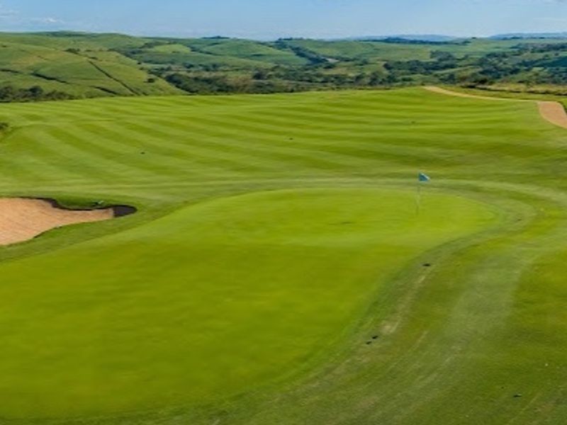 An elevated view of a well-maintained golf course green with a sand bunker and rolling hills in the background.