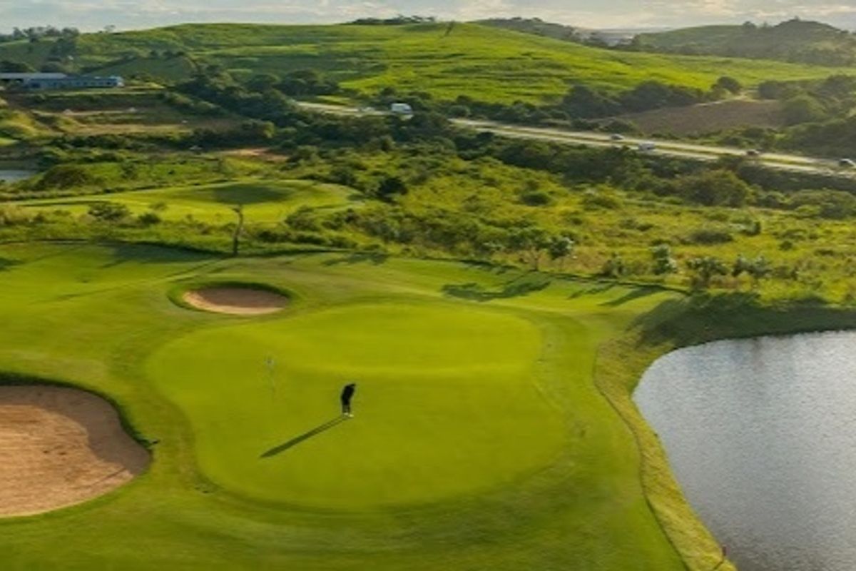 Aerial view of a well-maintained golf course featuring manicured greens, sand bunkers, and a water hazard set against a scenic landscape.