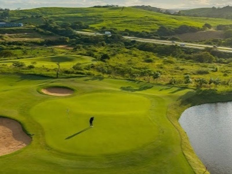 Aerial view of a well-maintained golf course featuring manicured greens, sand bunkers, and a water hazard set against a scenic landscape.