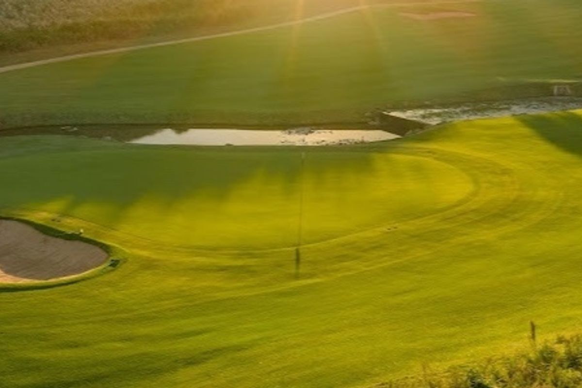 A scenic elevated view of a well-maintained golf course featuring a sand bunker and a water hazard at sunset.