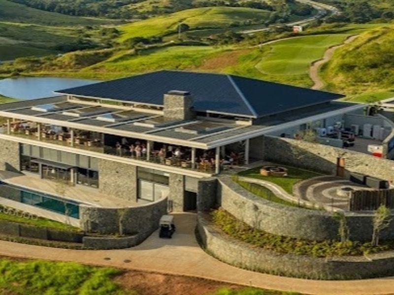 Aerial view of a modern clubhouse featuring stone-clad architecture, a swimming pool, and landscaped terraces overlooking a golf course.