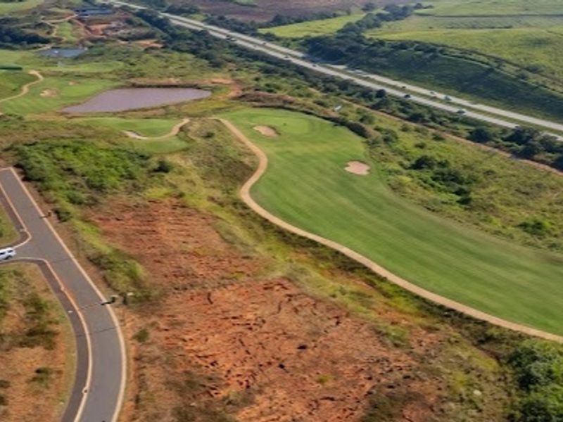 Aerial view of a vacant residential plot situated adjacent to a golf course and paved access road.
