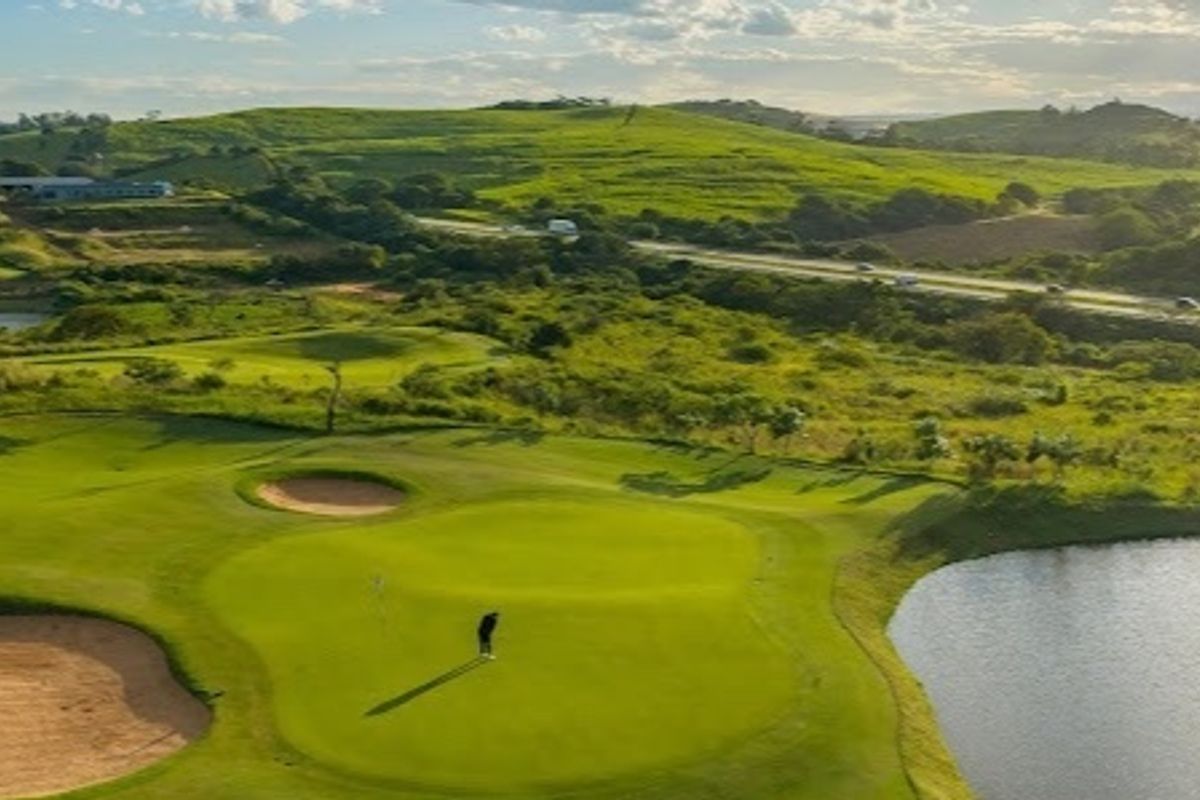 An aerial view of a well-maintained golf course featuring lush green fairways, sand bunkers, and a water hazard set against a scenic landscape.