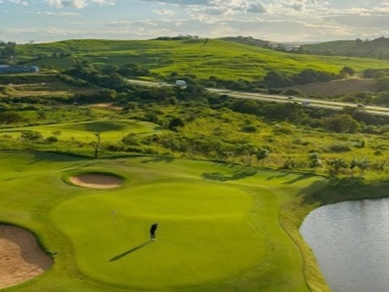 An aerial view of a well-maintained golf course featuring lush green fairways, sand bunkers, and a water hazard set against a scenic landscape.