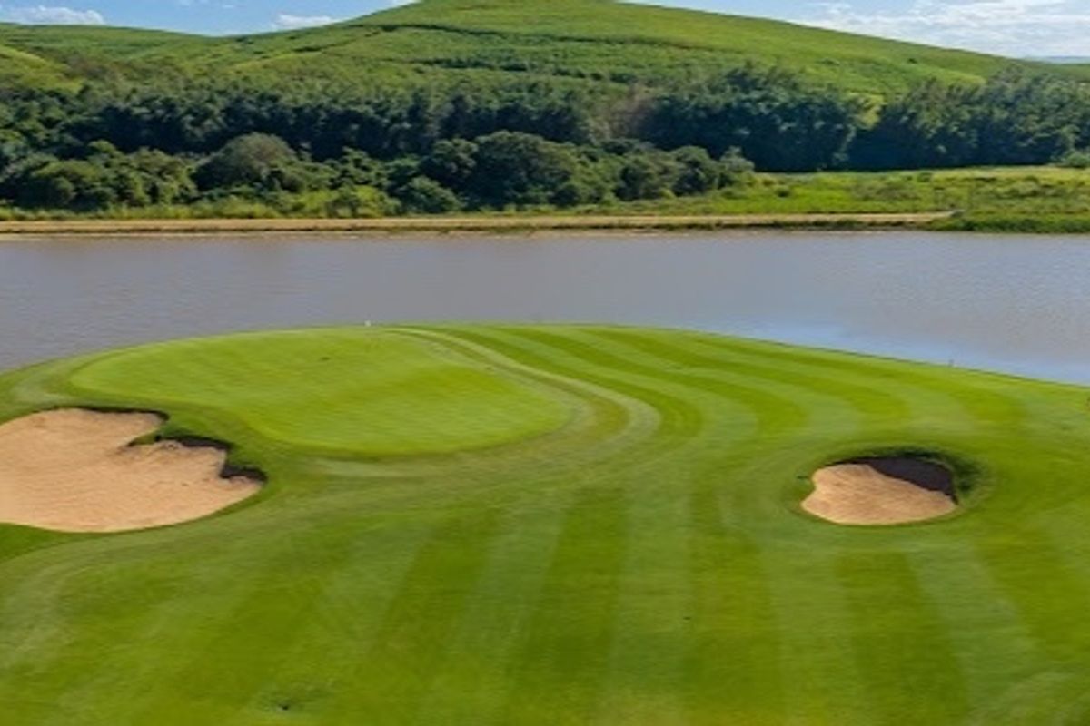 Aerial view of a manicured golf course green featuring sand bunkers, overlooking a scenic lake and rolling hills.