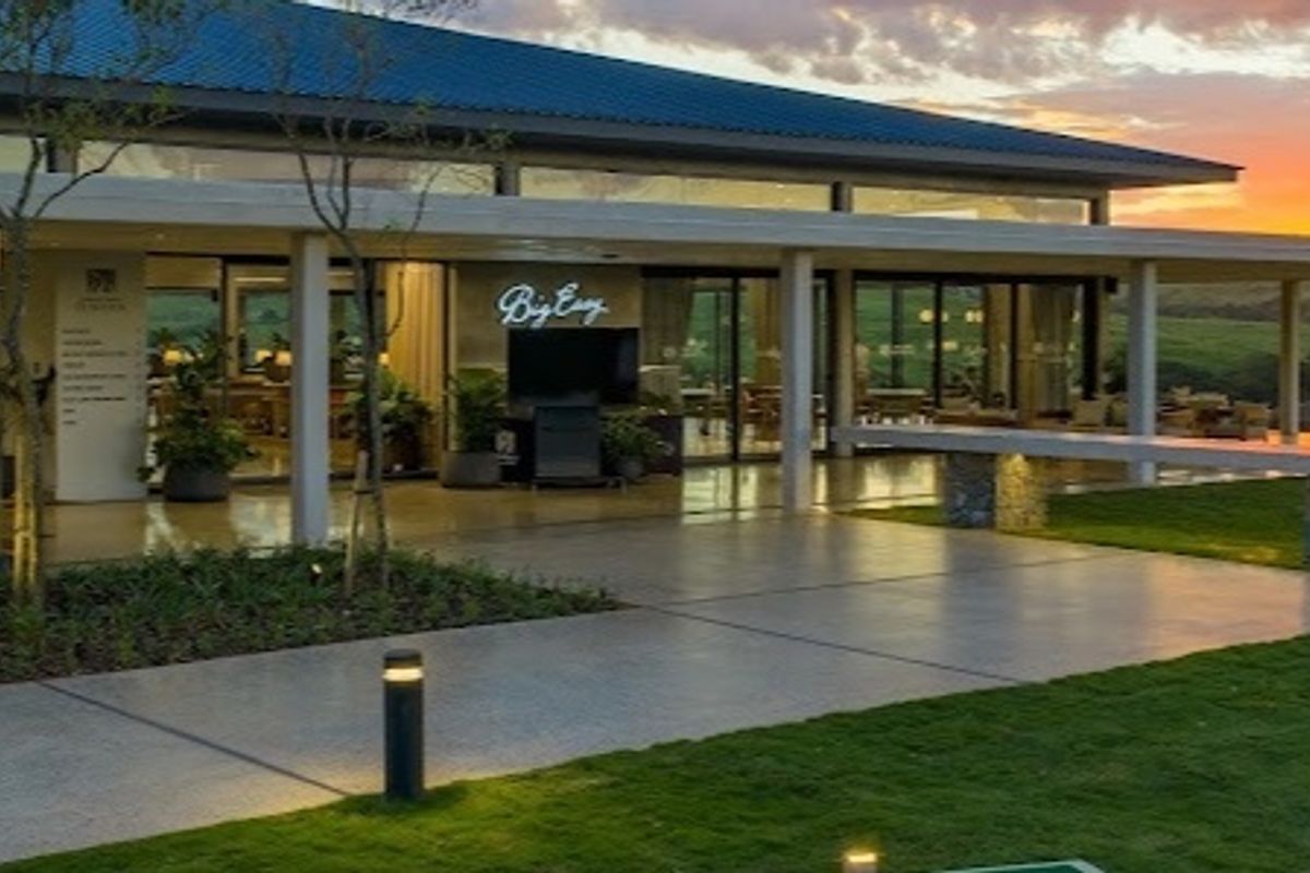 A spacious covered patio area featuring stone pillars, recessed lighting, and large glass sliding doors, overlooking a well-maintained garden at sunset.