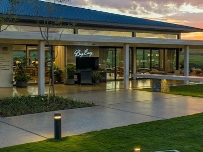 A spacious covered patio area featuring stone pillars, recessed lighting, and large glass sliding doors, overlooking a well-maintained garden at sunset.