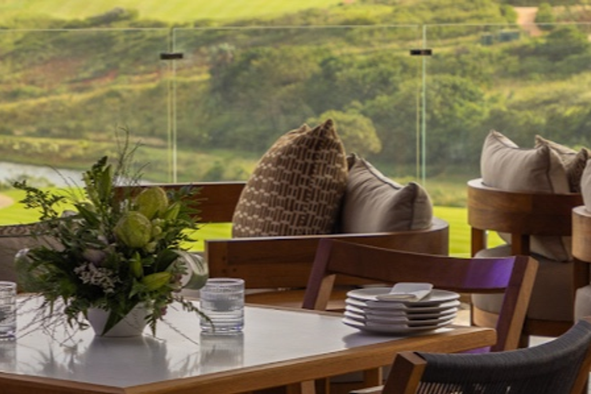 A scenic outdoor patio area featuring a modern glass balustrade overlooking a lush green landscape and water feature.