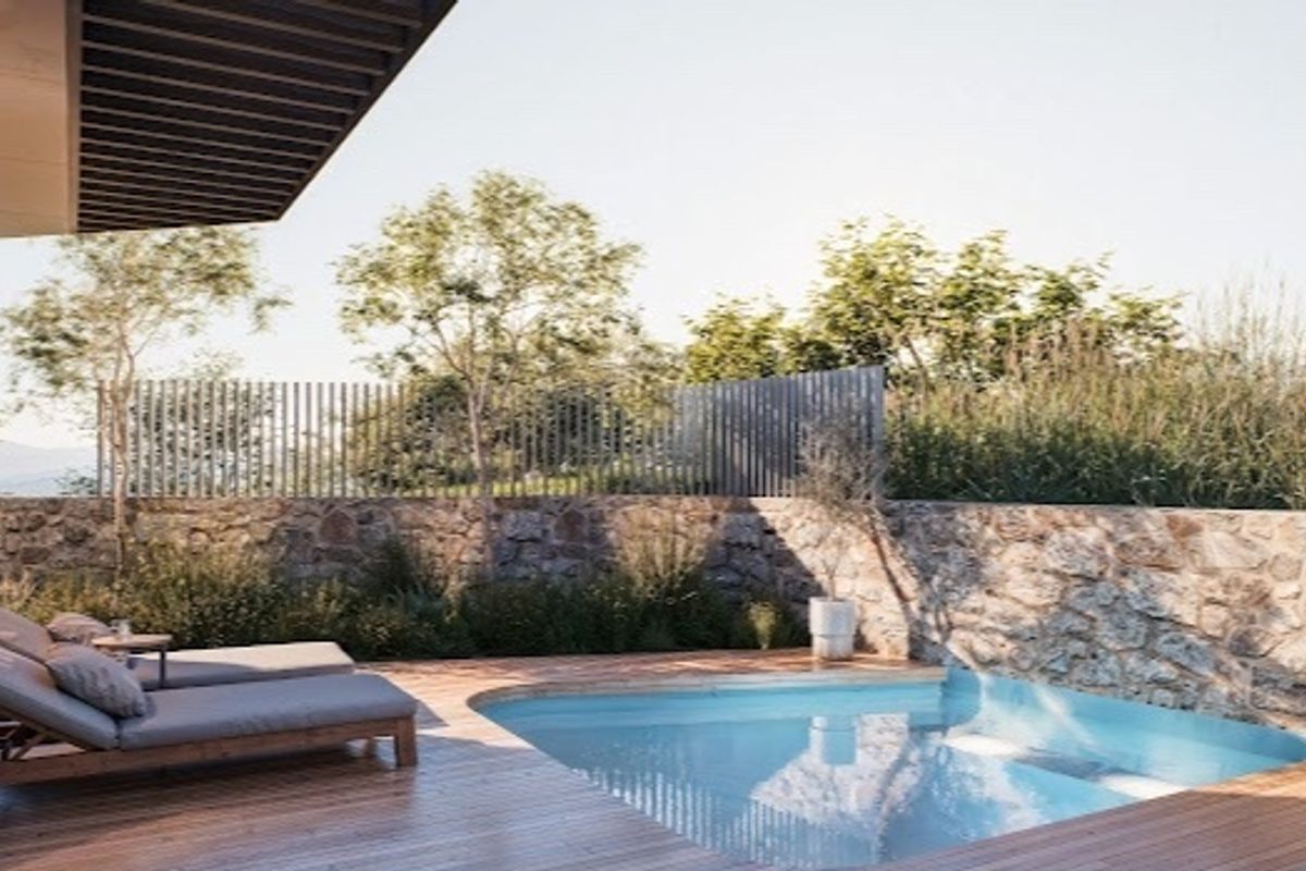 A modern outdoor pool area featuring timber decking, a stone retaining wall, and a sleek swimming pool set against a landscaped backdrop.