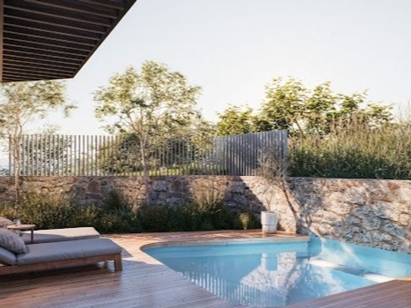 A modern outdoor pool area featuring timber decking, a stone retaining wall, and a sleek swimming pool set against a landscaped backdrop.