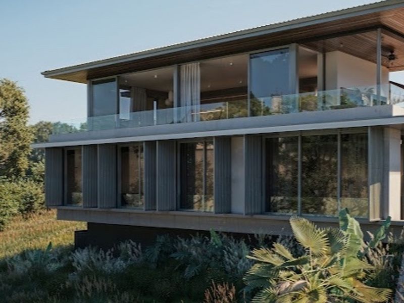 A modern multi-level residential property featuring expansive glass sliding doors, a glass balustrade, and a timber-lined overhanging roof set within a landscaped environment.