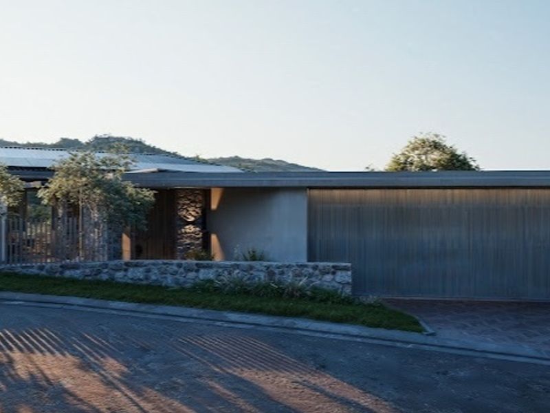 Modern residential facade featuring stone cladding, a sleek metal garage door, and a paved driveway in a scenic hillside setting.
