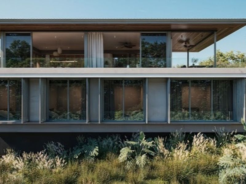 A modern two-story residential structure featuring expansive glass sliding doors, a glass balustrade, and deep roof eaves, set within a natural landscape.
