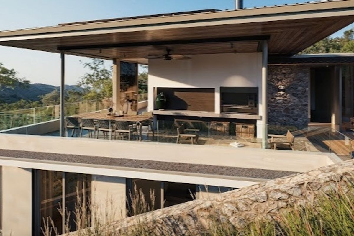 A modern covered patio featuring a built-in braai, timber ceiling, and glass balustrades, offering an elevated outdoor entertainment space with scenic views.