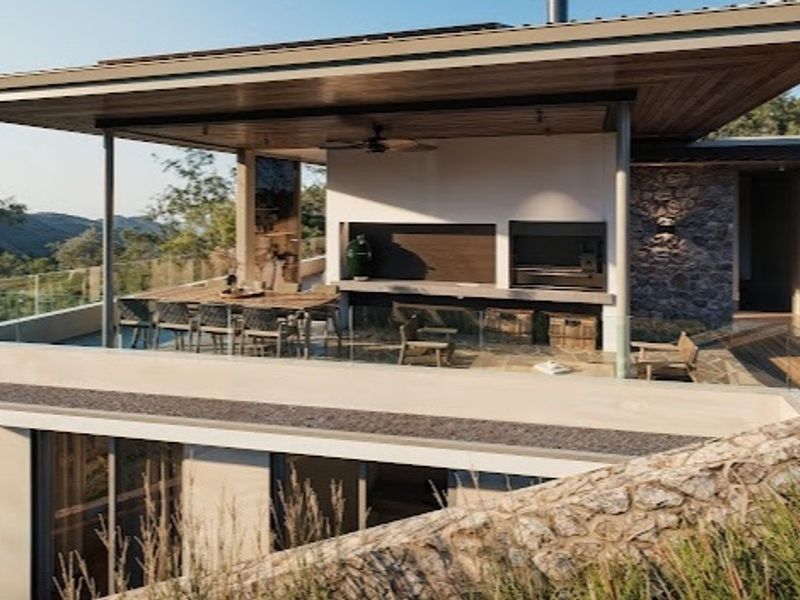 A modern covered patio featuring a built-in braai, timber ceiling, and glass balustrades, offering an elevated outdoor entertainment space with scenic views.