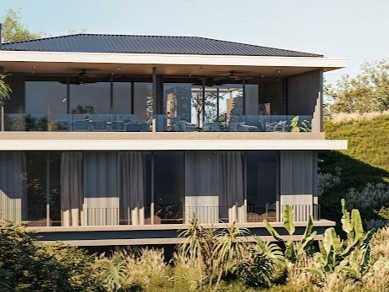 A modern two-story residential structure featuring expansive glass sliding doors, covered balconies with glass balustrades, and a sleek metal roof set in a natural landscape.