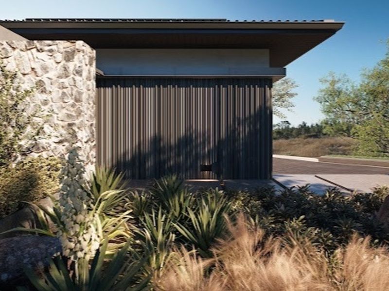 A modern residential exterior featuring stone cladding, vertical metal siding, and a deep roof overhang, set within a landscaped garden.