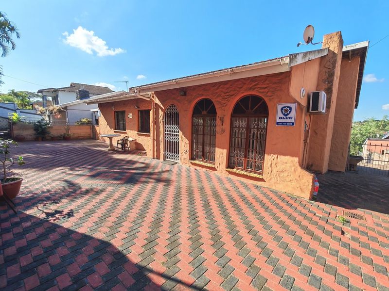 Rear exterior view of the house featuring a large paved courtyard, arched windows with security gates, and a textured stucco finish.