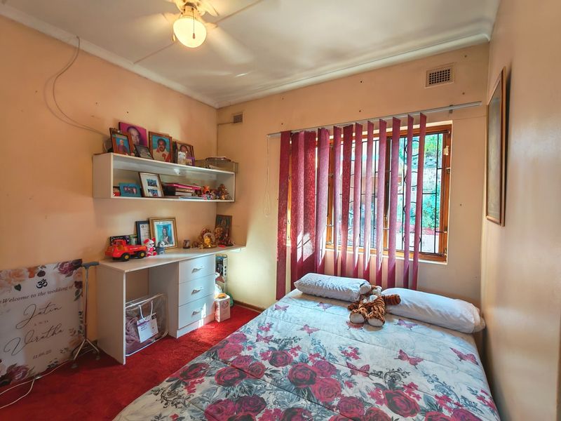 A bedroom featuring a built-in desk and shelving unit, a window with security bars, and a ceiling light fixture.