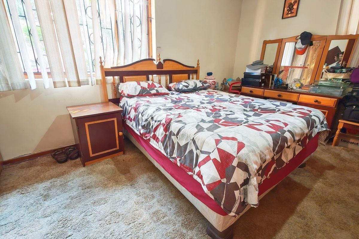 A bedroom featuring carpet flooring and a window fitted with security bars, offering a functional space ready for modernization.