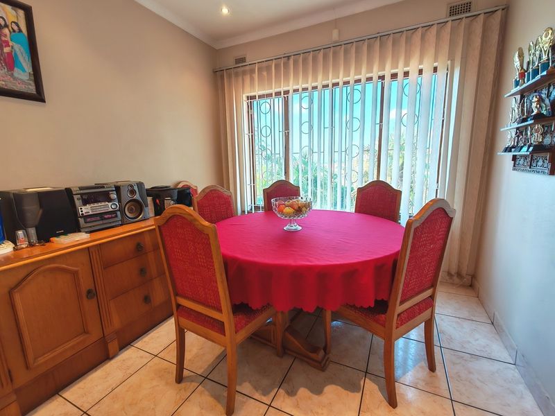 A functional dining room featuring tiled flooring, recessed lighting, and large windows fitted with vertical blinds and security bars.