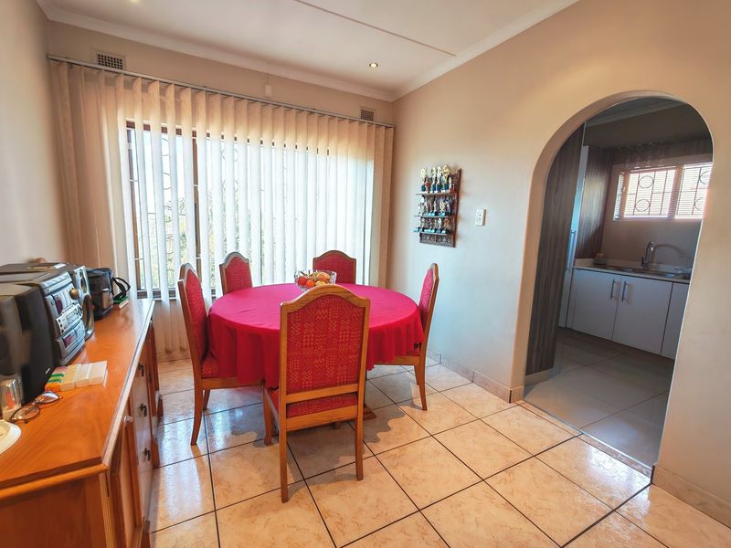 Dining room featuring tiled flooring and an arched entryway leading to the kitchen, with natural light provided by large windows with vertical blinds.
