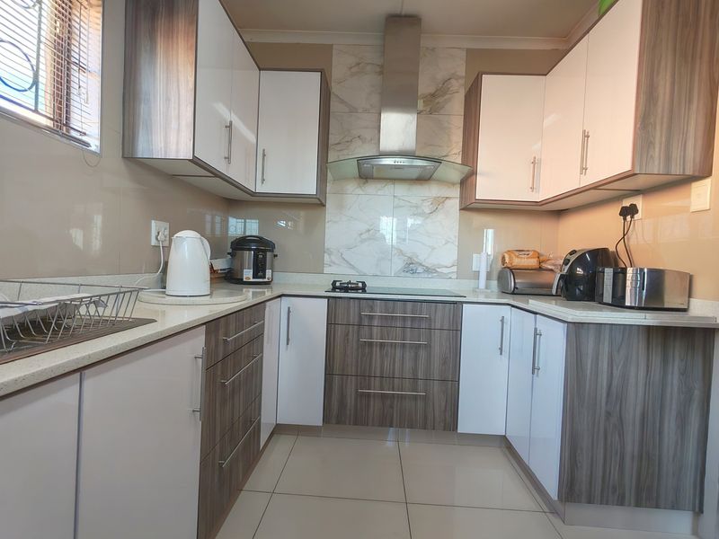 Modern kitchen featuring two-tone cabinetry, stone countertops, a tiled splashback, and a built-in hob with an extractor fan.