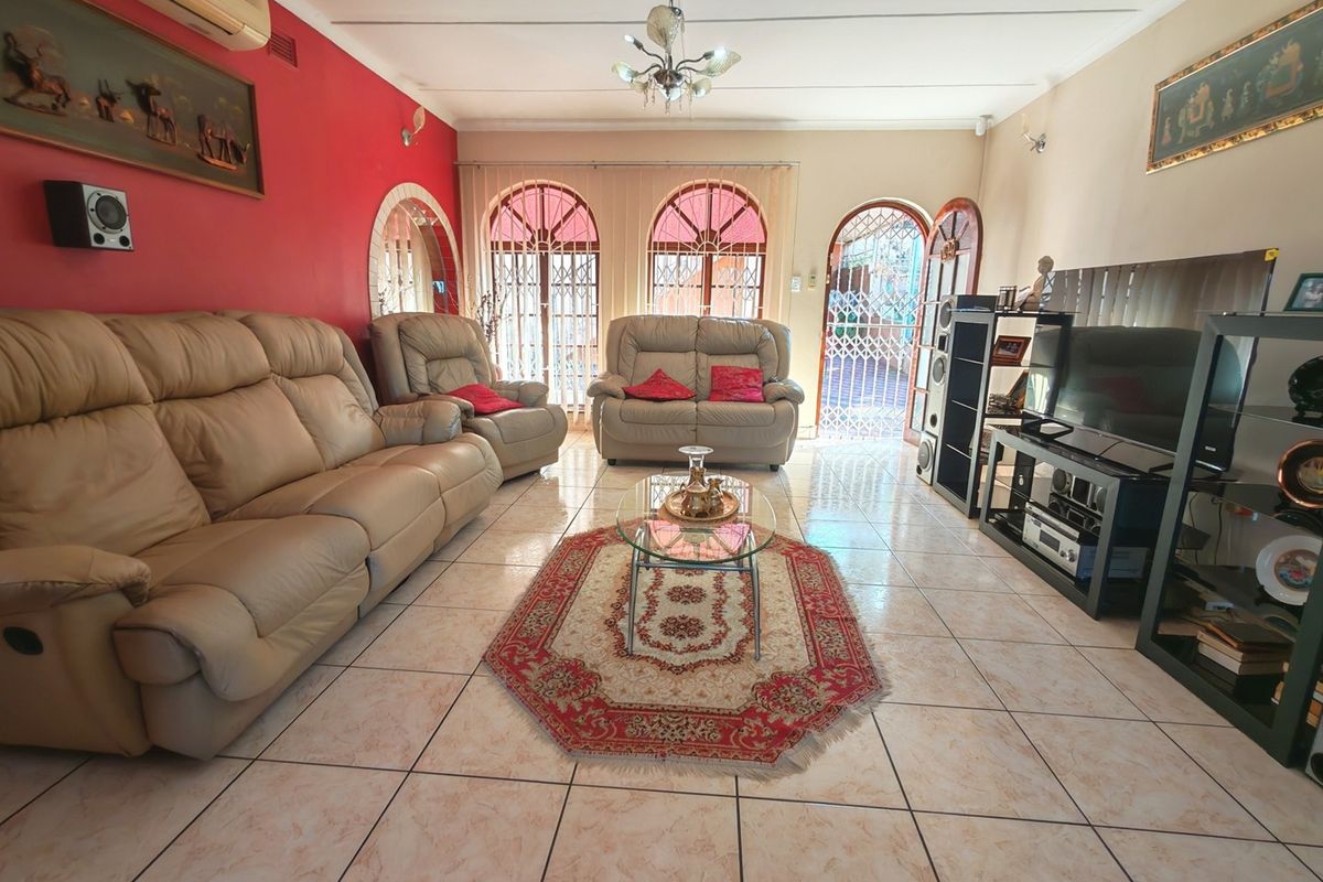 A spacious living room featuring tiled flooring, arched windows with security gates, and an integrated air conditioning unit.