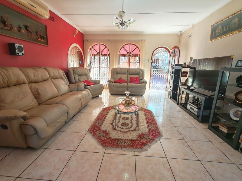 A spacious living room featuring tiled flooring, arched windows with security gates, and an integrated air conditioning unit.
