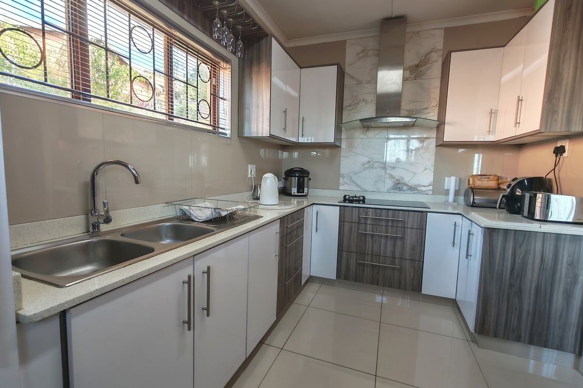 Modern kitchen featuring two-tone cabinetry, stone countertops, a double basin sink, and a stainless steel extractor fan with marble-look splashback.