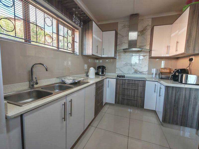 Modern kitchen featuring two-tone cabinetry, stone countertops, a double basin sink, and a stainless steel extractor fan with marble-look splashback.