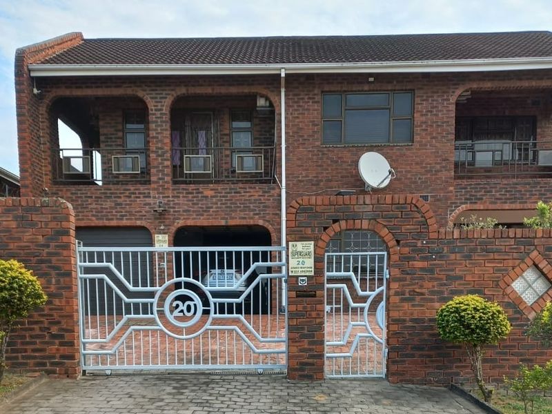 Front elevation of a double-story face brick house featuring a secure gated entrance, integrated garage, and upper-level balcony.