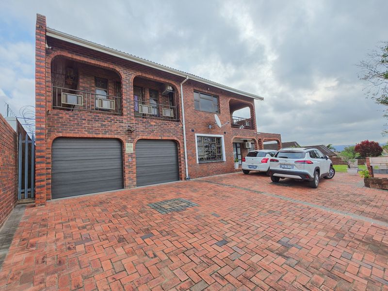 A double-story face brick residence featuring a paved driveway, double garage, and an upper-level balcony with integrated security features.