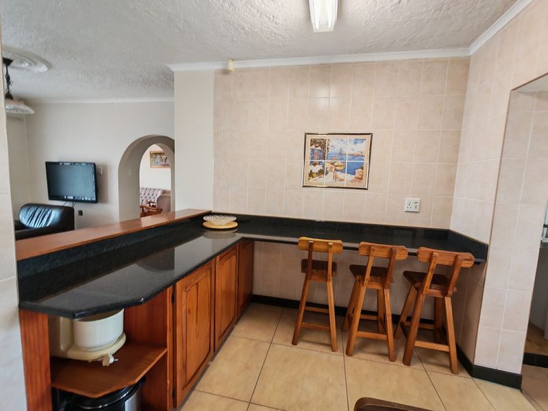 Open plan kitchen area featuring granite countertops, wooden cabinetry, and tiled finishes, seamlessly connecting to the adjacent living space through an archway.