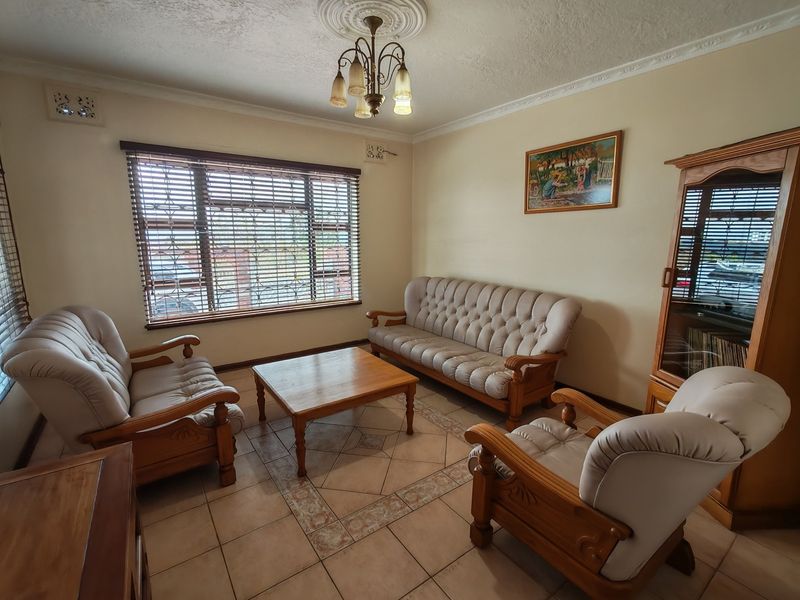 A well-maintained living room featuring ceramic floor tiles, decorative ceiling cornice, and secure window treatments with burglar bars.