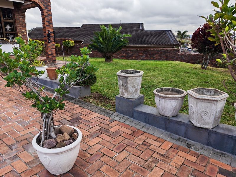 A well-maintained rear garden featuring a brick-paved patio, a low brick retaining wall, and established landscaping with a view of the neighboring property.