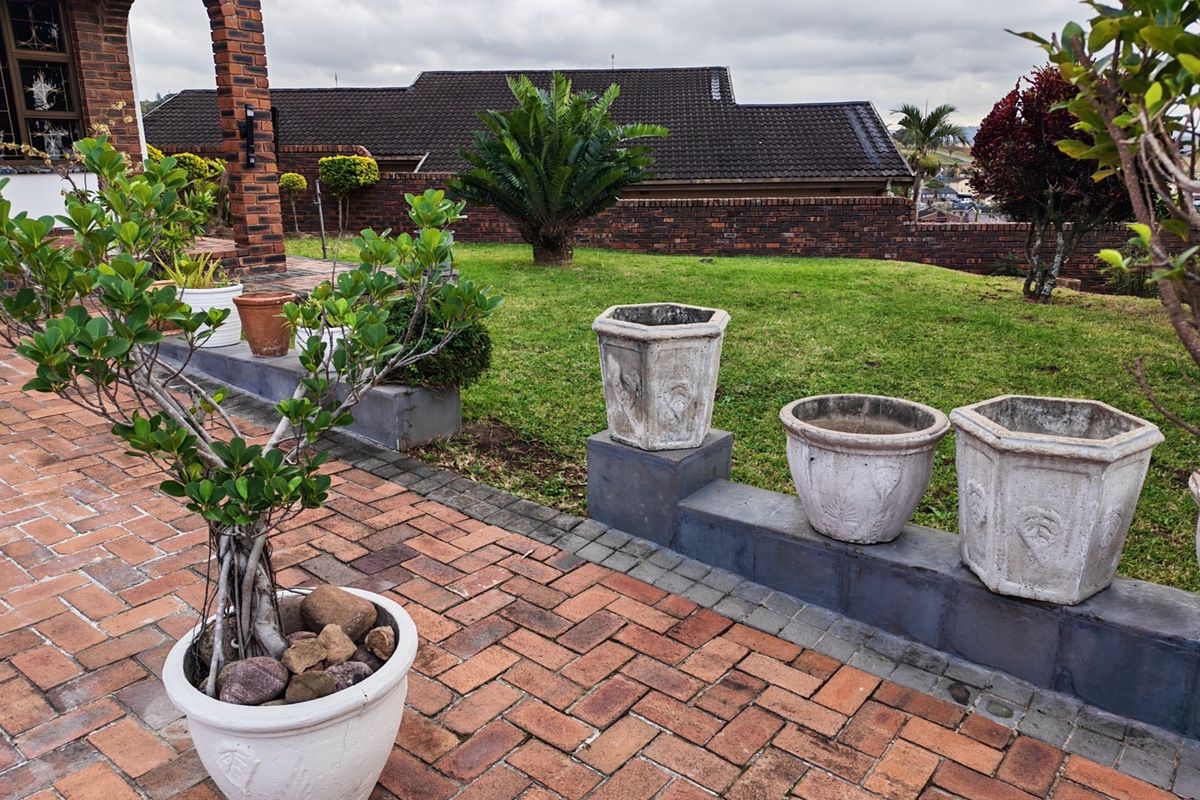 A well-maintained rear garden featuring a brick-paved patio, a low brick retaining wall, and established landscaping with a view of the neighboring property.