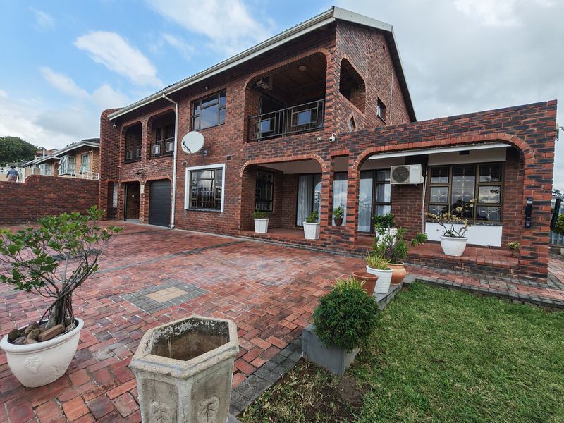 A double-story face brick house featuring an arched covered patio, balcony, paved driveway, and integrated garage.