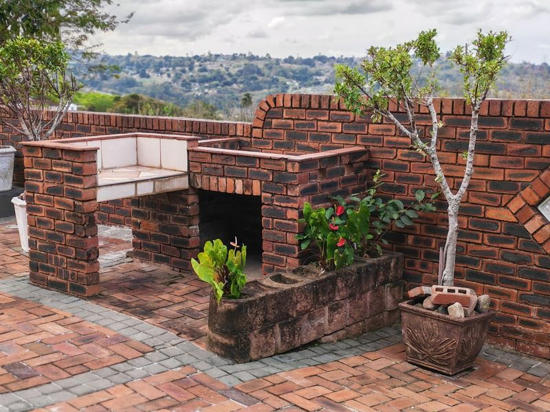 Outdoor patio area featuring a built-in brick braai, brick paving, and a low brick boundary wall with scenic landscape views.