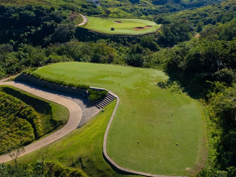 Aerial view of a well-maintained residential plot featuring landscaped lawns, stone retaining walls, and a concrete pathway set within a lush green environment.